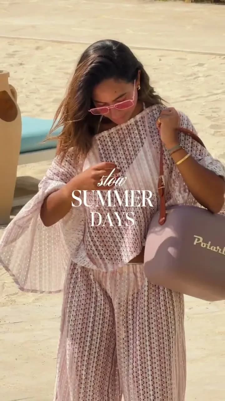 Model in a pink knit cover-up with a lilac shoulder bag on the beach